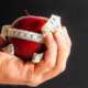 Person holding red apple with tape measure around it.